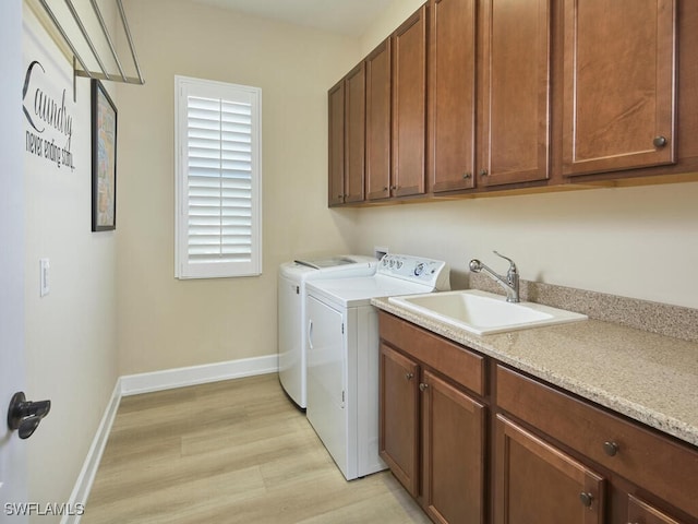 laundry room featuring washer and clothes dryer, light hardwood / wood-style floors, cabinets, and sink