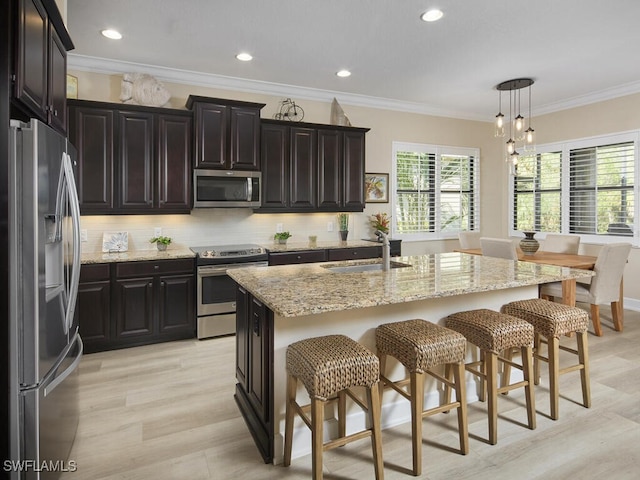 kitchen featuring a kitchen breakfast bar, stainless steel appliances, a kitchen island with sink, sink, and decorative light fixtures