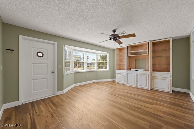 unfurnished living room featuring built in shelves, a textured ceiling, light hardwood / wood-style floors, and ceiling fan