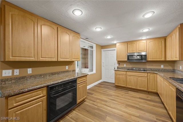 kitchen with light brown cabinets, dark stone counters, black appliances, sink, and light wood-type flooring