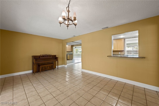 spare room featuring a textured ceiling, an inviting chandelier, and light tile patterned flooring