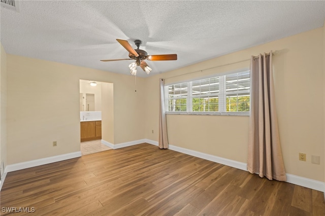 unfurnished bedroom with connected bathroom, ceiling fan, hardwood / wood-style floors, and a textured ceiling