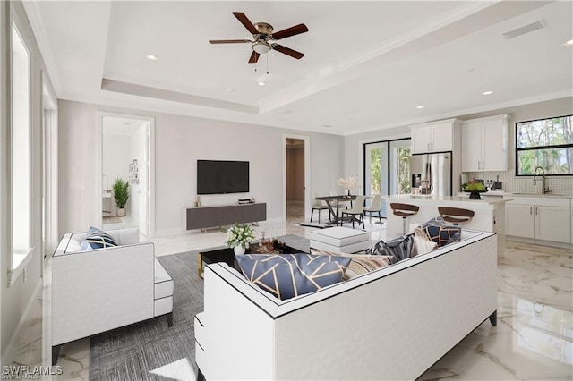 living room featuring a raised ceiling, ceiling fan, and sink