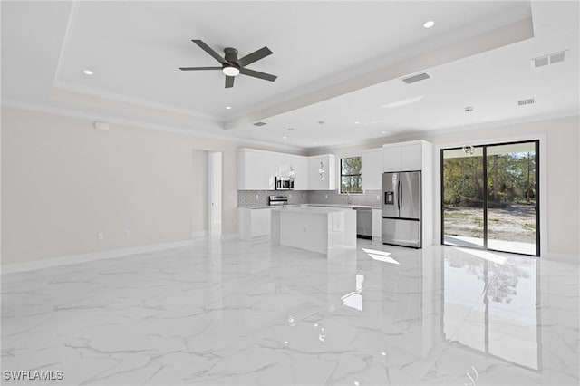 kitchen with crown molding, appliances with stainless steel finishes, white cabinetry, a kitchen island, and a raised ceiling