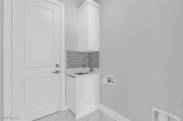 washroom featuring cabinet space, baseboards, marble finish floor, hookup for a washing machine, and a sink