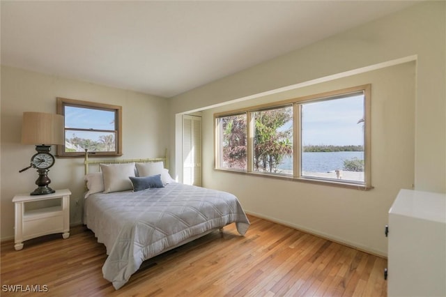 bedroom featuring multiple windows, a water view, and light wood-type flooring