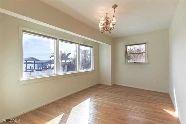 empty room with plenty of natural light, light hardwood / wood-style flooring, and an inviting chandelier