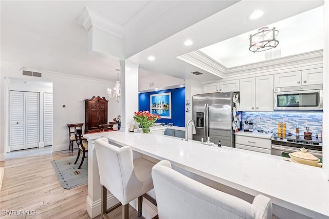 kitchen featuring a breakfast bar area, a chandelier, white cabinets, stainless steel appliances, and backsplash