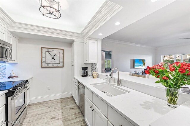 kitchen with sink, ornamental molding, stainless steel appliances, light stone countertops, and white cabinets