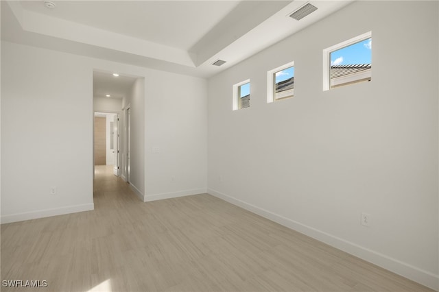 unfurnished room with a tray ceiling, a wealth of natural light, and light wood-type flooring