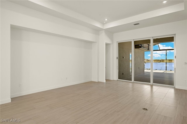 spare room with a water view, light hardwood / wood-style flooring, and a tray ceiling