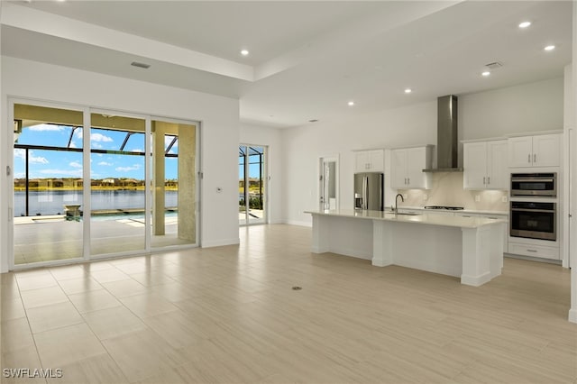 kitchen featuring white cabinets, a water view, wall chimney range hood, a large island, and stainless steel appliances