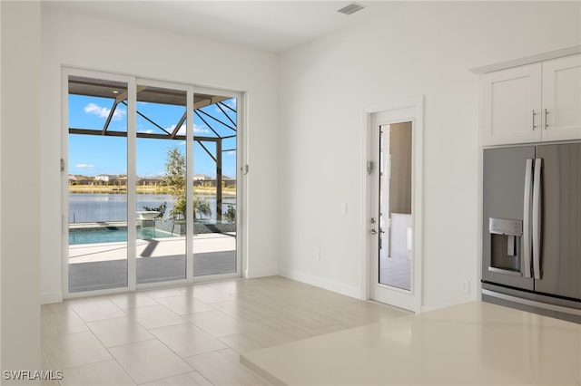 interior space featuring a water view, stainless steel fridge with ice dispenser, white cabinets, and light tile patterned floors