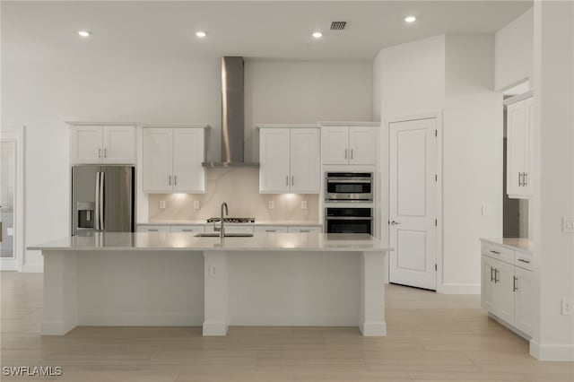 kitchen featuring sink, wall chimney range hood, a center island with sink, white cabinets, and appliances with stainless steel finishes