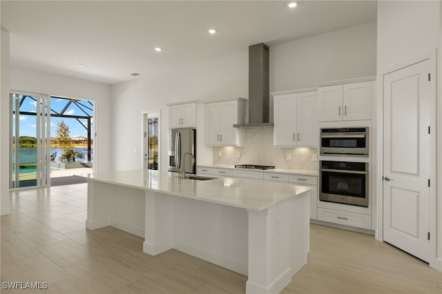 kitchen with a kitchen island with sink, sink, wall chimney exhaust hood, white cabinetry, and stainless steel appliances