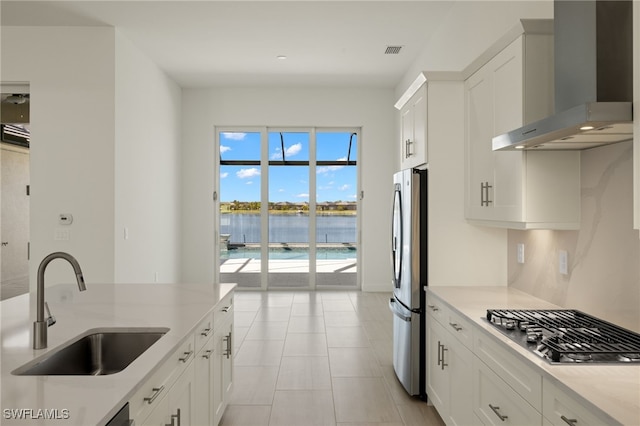 kitchen with appliances with stainless steel finishes, wall chimney exhaust hood, sink, a water view, and white cabinets