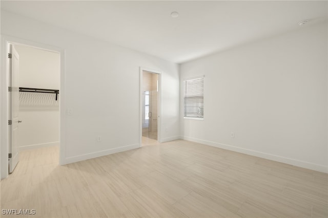 unfurnished bedroom featuring connected bathroom, light hardwood / wood-style floors, a spacious closet, and a closet