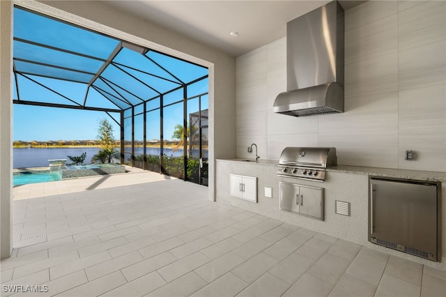 view of patio / terrace with a lanai, sink, exterior kitchen, a water view, and grilling area