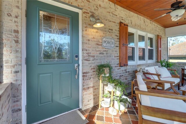 doorway to property with ceiling fan, a porch, and brick siding