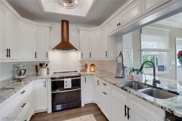 kitchen featuring range with two ovens, dark wood-style flooring, white cabinets, a sink, and wall chimney range hood