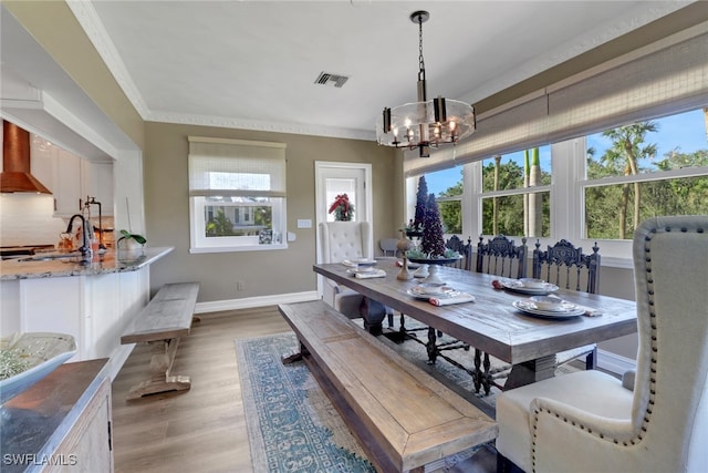 dining space with a healthy amount of sunlight, visible vents, crown molding, and light wood-style flooring