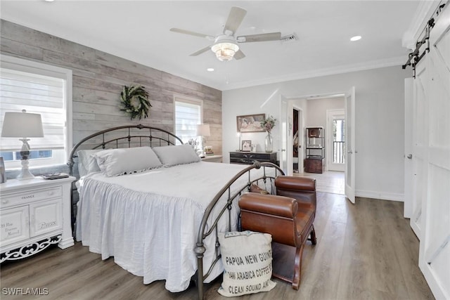 bedroom with ornamental molding, wood finished floors, baseboards, and a barn door