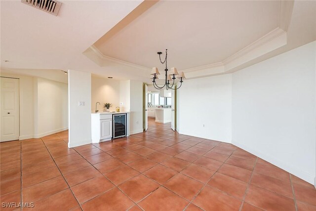 unfurnished dining area with sink, a raised ceiling, wine cooler, a notable chandelier, and ornamental molding