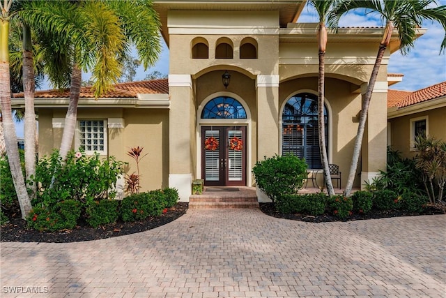 entrance to property featuring a tile roof, french doors, and stucco siding