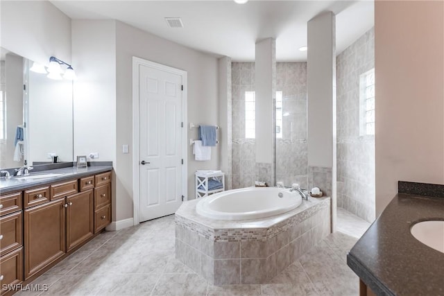 bathroom featuring tile patterned flooring, vanity, and a relaxing tiled tub