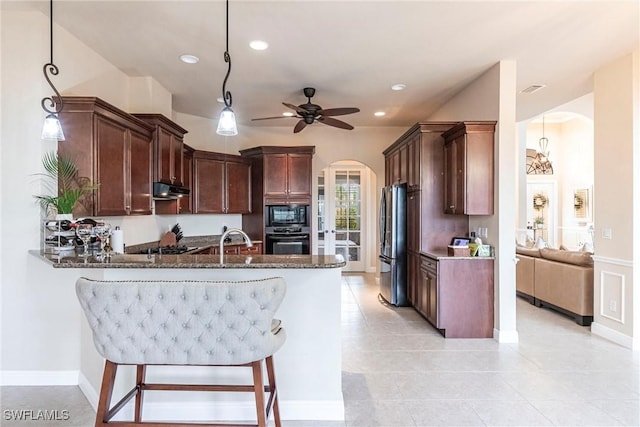 kitchen featuring arched walkways, hanging light fixtures, dark stone counters, a peninsula, and black appliances