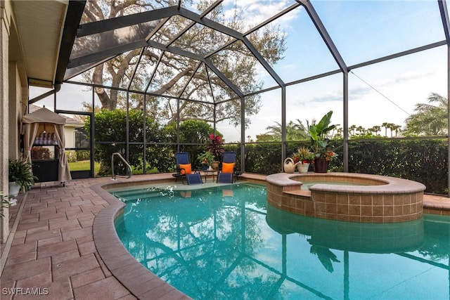 outdoor pool with glass enclosure, a patio area, and an in ground hot tub