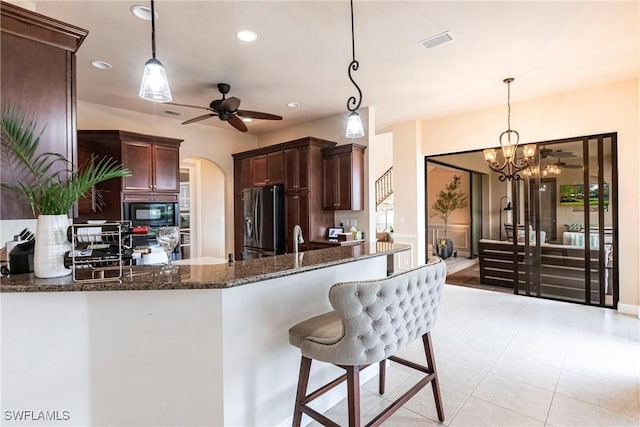 kitchen featuring stainless steel fridge, arched walkways, dark stone counters, black microwave, and pendant lighting