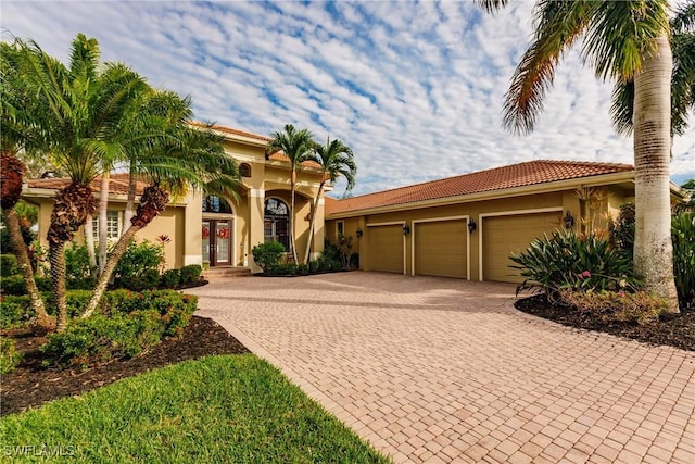 mediterranean / spanish-style home featuring decorative driveway, an attached garage, a tile roof, and stucco siding