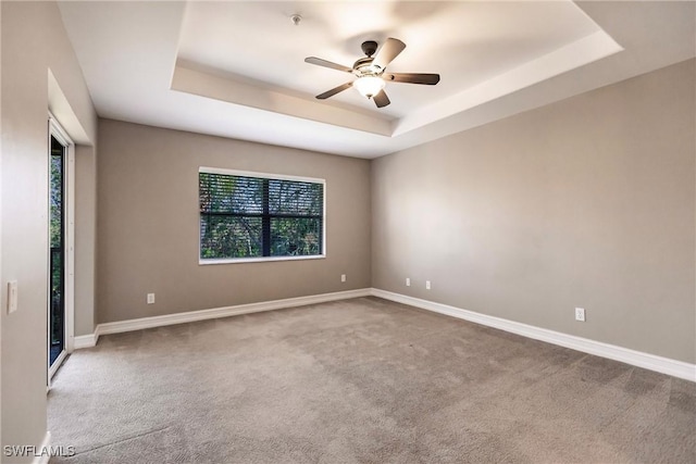 carpeted spare room with ceiling fan and a tray ceiling