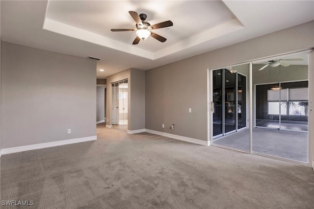 carpeted spare room featuring a tray ceiling and ceiling fan