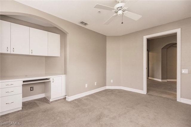 unfurnished office featuring built in desk, light colored carpet, and ceiling fan