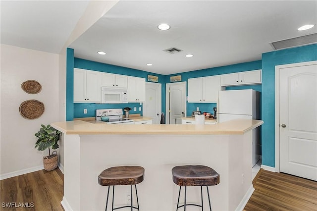 kitchen featuring white appliances, a kitchen breakfast bar, kitchen peninsula, dark hardwood / wood-style floors, and white cabinetry