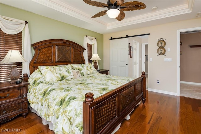 bedroom with dark wood-type flooring, ceiling fan, a barn door, ornamental molding, and a tray ceiling