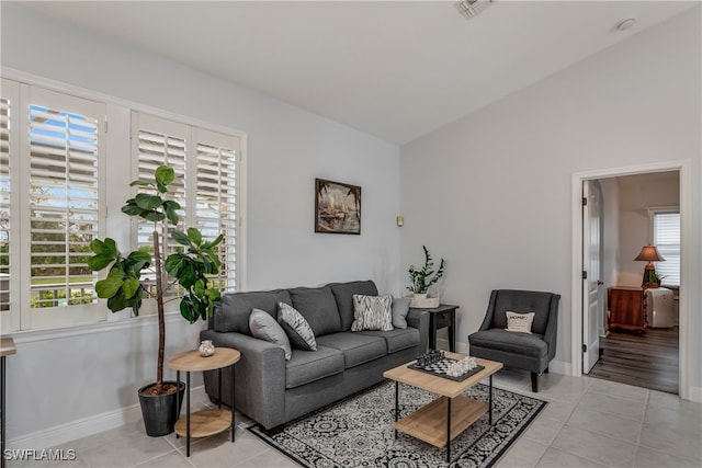 living room featuring light tile patterned floors, vaulted ceiling, visible vents, and baseboards