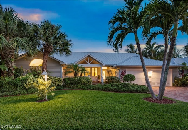 ranch-style home with a garage, metal roof, decorative driveway, and a front yard