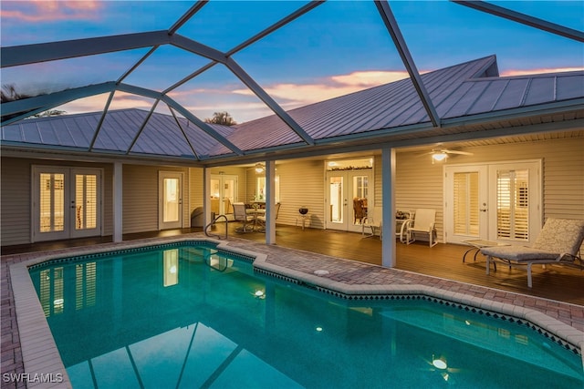 pool at dusk with a deck, french doors, ceiling fan, and glass enclosure