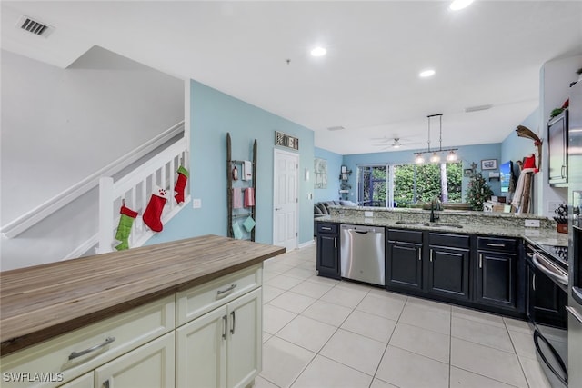 kitchen featuring sink, butcher block countertops, decorative light fixtures, light tile patterned floors, and appliances with stainless steel finishes