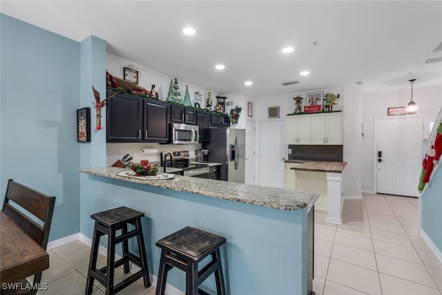 kitchen with appliances with stainless steel finishes, white cabinetry, a kitchen bar, light tile patterned floors, and kitchen peninsula