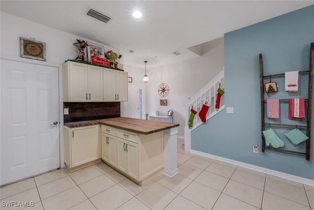 kitchen with butcher block counters, backsplash, hanging light fixtures, light tile patterned floors, and kitchen peninsula