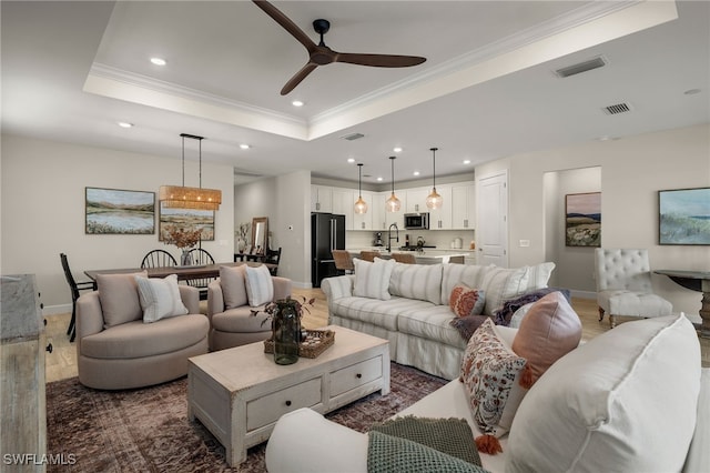 living room featuring ceiling fan, sink, a raised ceiling, dark hardwood / wood-style flooring, and ornamental molding