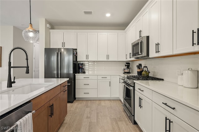 kitchen featuring white cabinetry, sink, stainless steel appliances, light stone counters, and pendant lighting