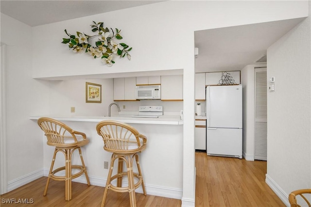 kitchen with kitchen peninsula, a kitchen breakfast bar, light wood-type flooring, white appliances, and white cabinetry