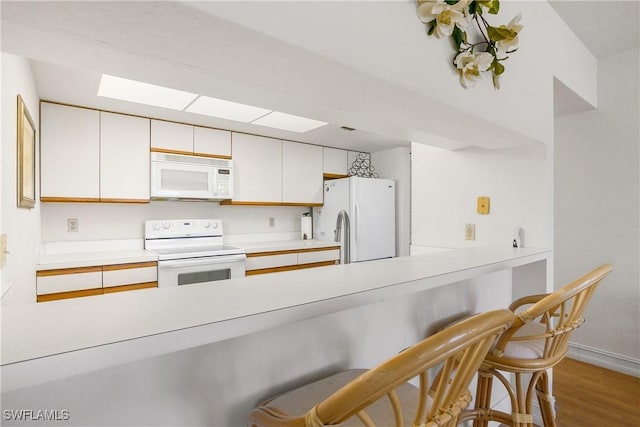 kitchen featuring kitchen peninsula, a kitchen breakfast bar, light wood-type flooring, white appliances, and white cabinetry