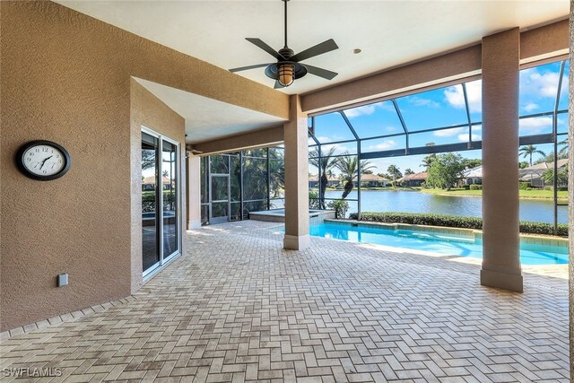 view of pool with glass enclosure, a water view, ceiling fan, and a patio area