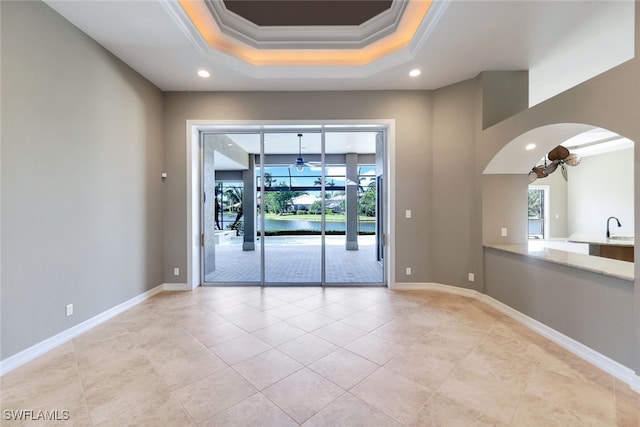 unfurnished room with light tile patterned floors, ceiling fan, a raised ceiling, ornamental molding, and sink